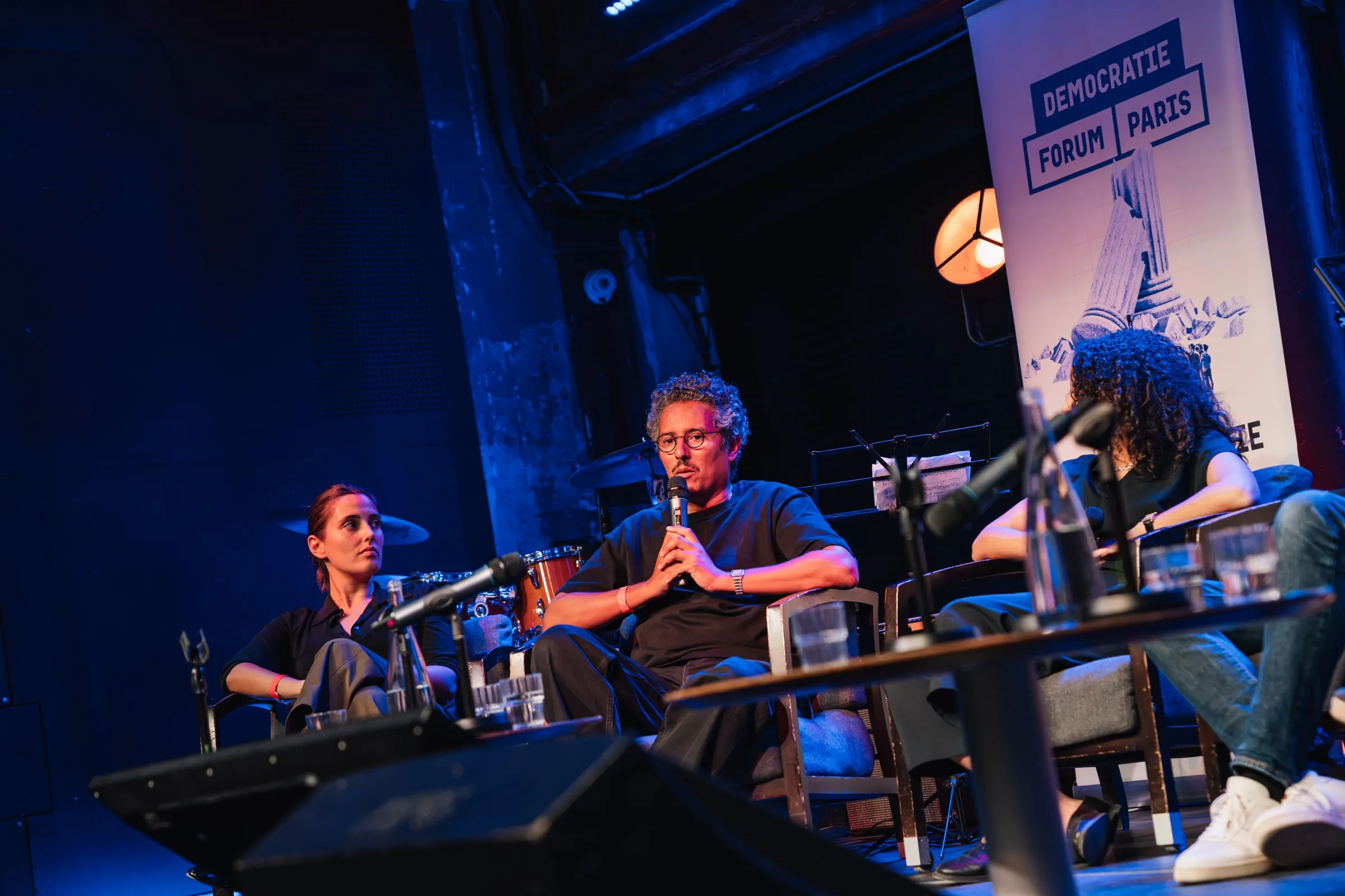 Un intervenant au micro pendant une table ronde, entouré de deux intervenantes.